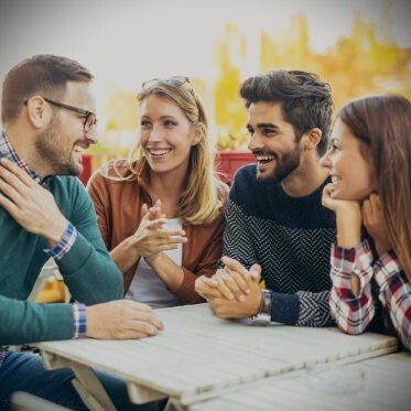 Group of four friends having fun a coffee together. Two women and two men at cafe talking laughing and enjoying their time