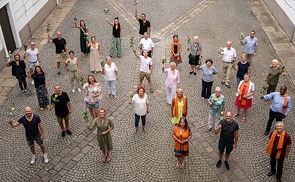 Eine Rose als Dankeschön: Ensemblemitglieder und MitarbeiterInnen des Linzer Musiktheaters mit Bischof Manfred Scheuer, Schwester Maria Schlackl und ihrem Team (alle mit orangefarbenem Schal) im Innenhof des Linzer Bischofshofs.