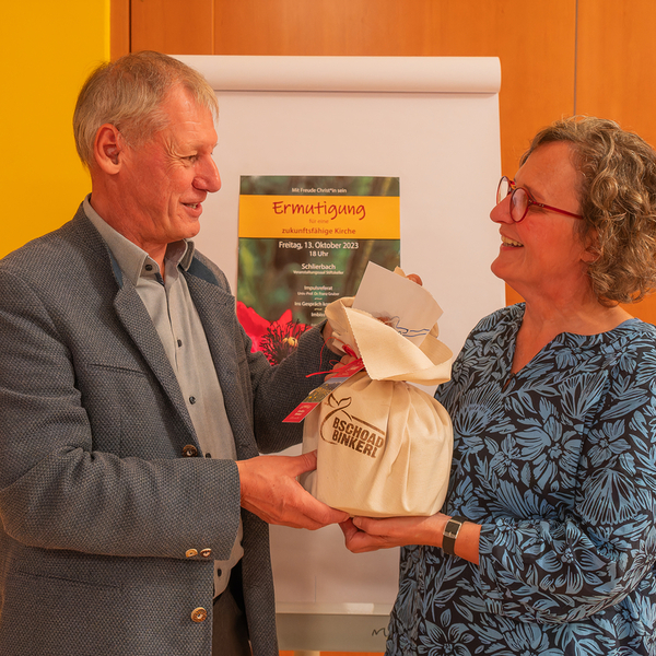 Univ.-Prof. Franz Gruber erhält von Dekanatsassistentin Susanne Lammer ein Bschoadbinkerl; Bschoad: 1) Jause für den Weg, den wir gehen 2) bescheiden -