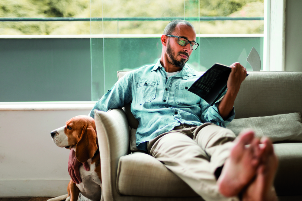 Ein Mann liest ein Buch und krault nebenbei seinen Hund