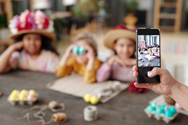 Close-up of woman making photo on her mobile phone of group of children sitting at the table during Easter