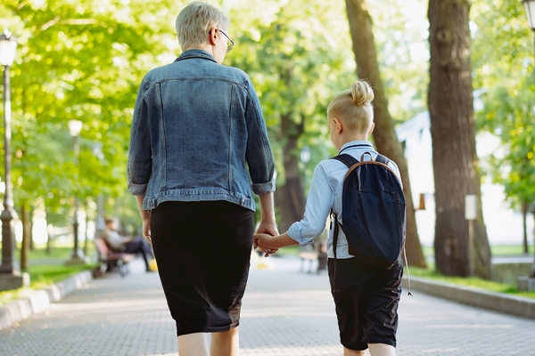 mother and son going to school holding hands. Caucasian blond boy with hairs tied up in ponytail looking at mom. Image with seective focus