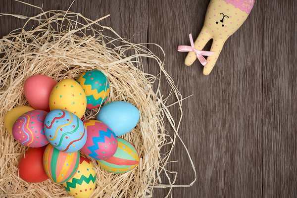 Easter eggs and rabbit. Happy bunny handmade and hand painted multicolored decorated eggs on straw nest, wooden background, copyspace. Unusual creative holiday greeting card 